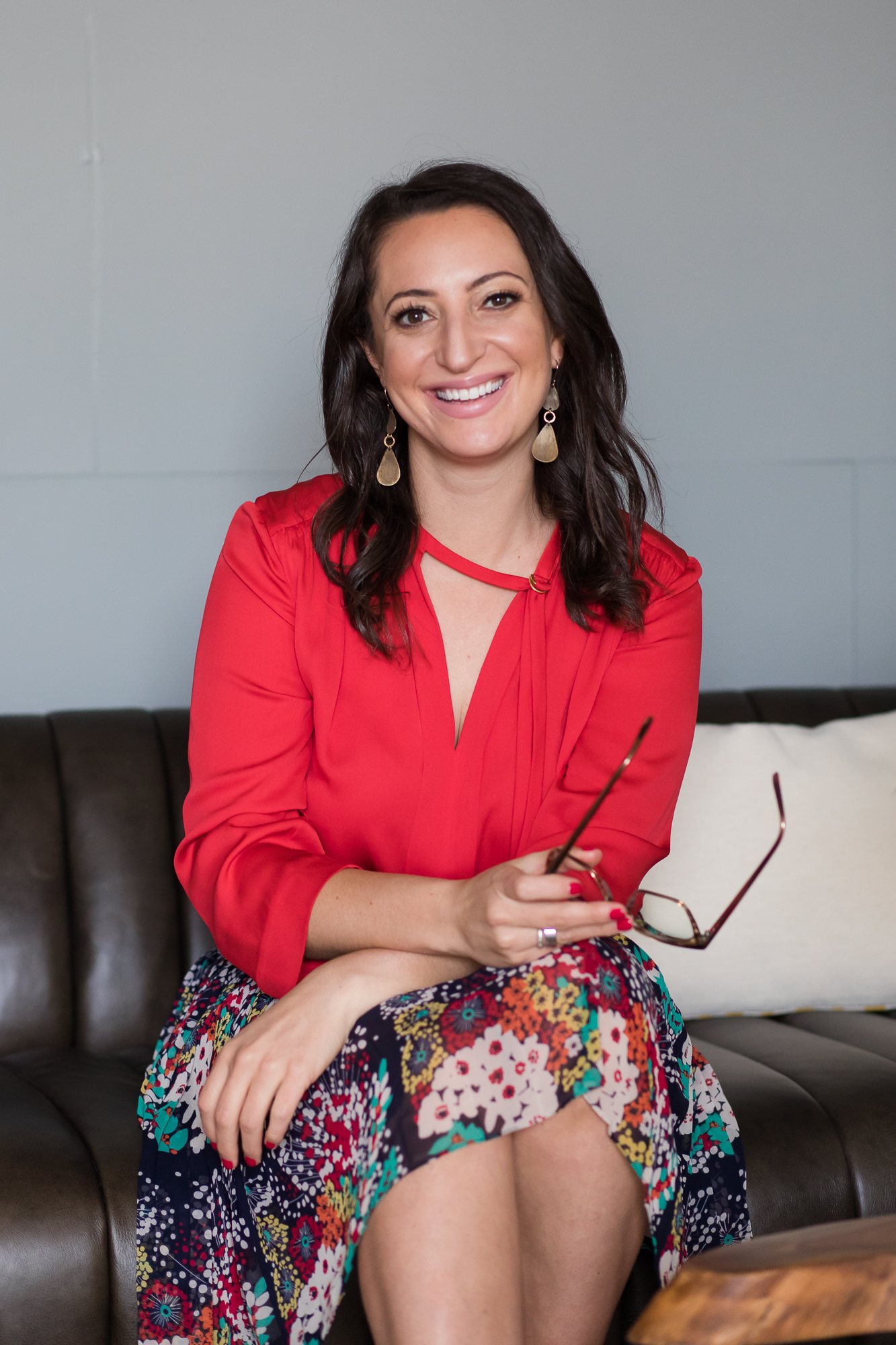 Lauren Goldstein, The Biz Doctor®, smiling on a leather sofa in a red blouse