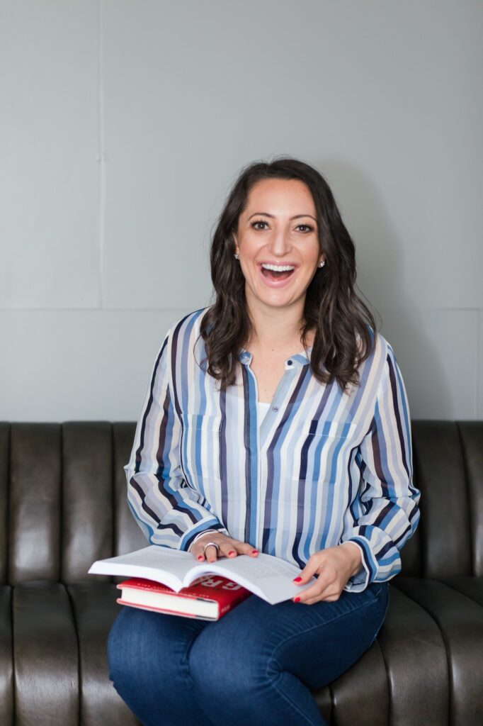 Lauren Goldstein laughing on a sofa with a book in her lap